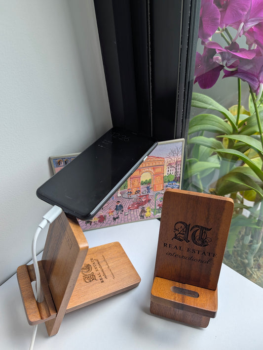 Wooden phone stands with engraved logos on a desk next to a laptop and plant.