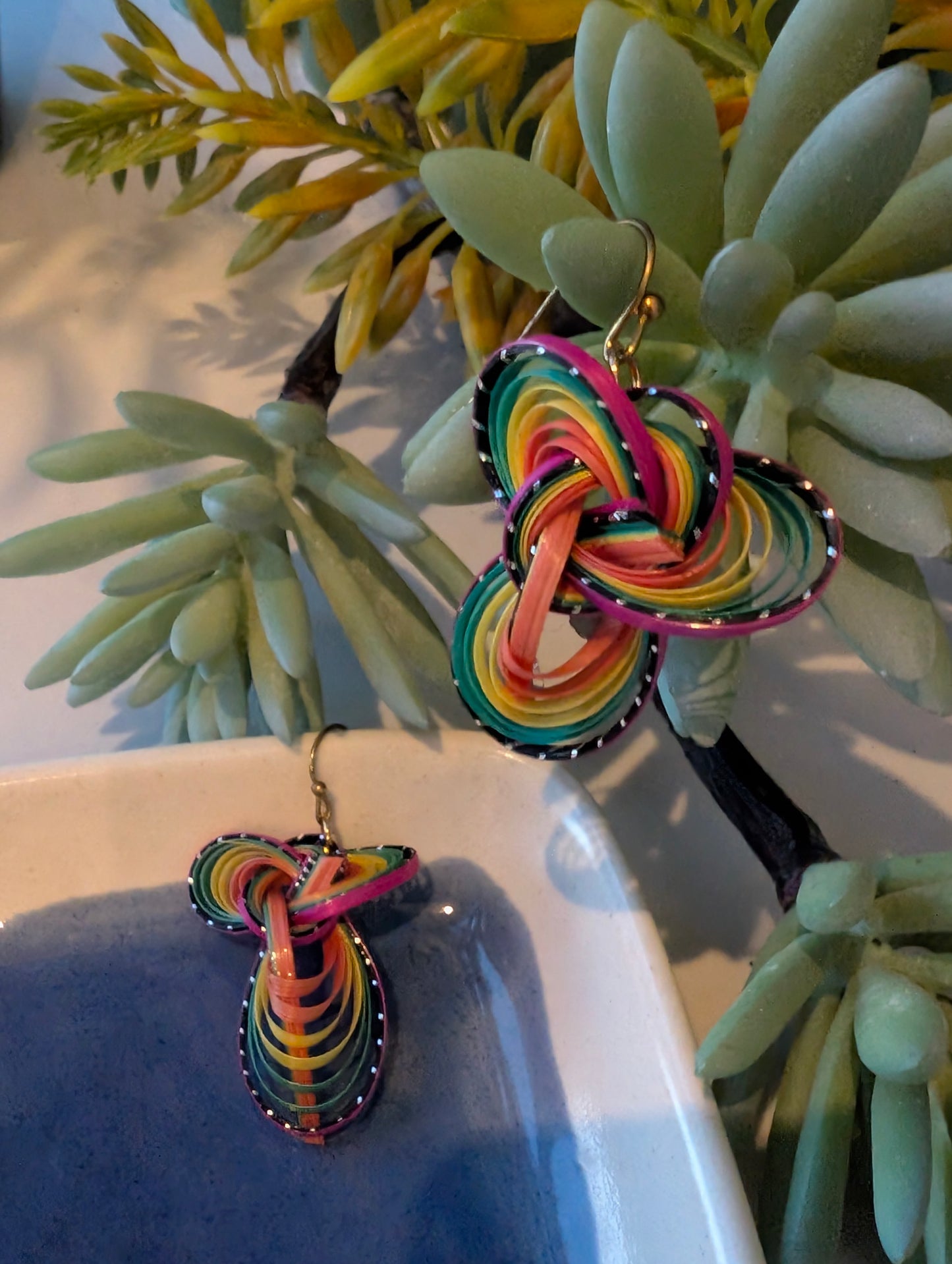 Colorful knotted earrings on a white surface with green plants in the background