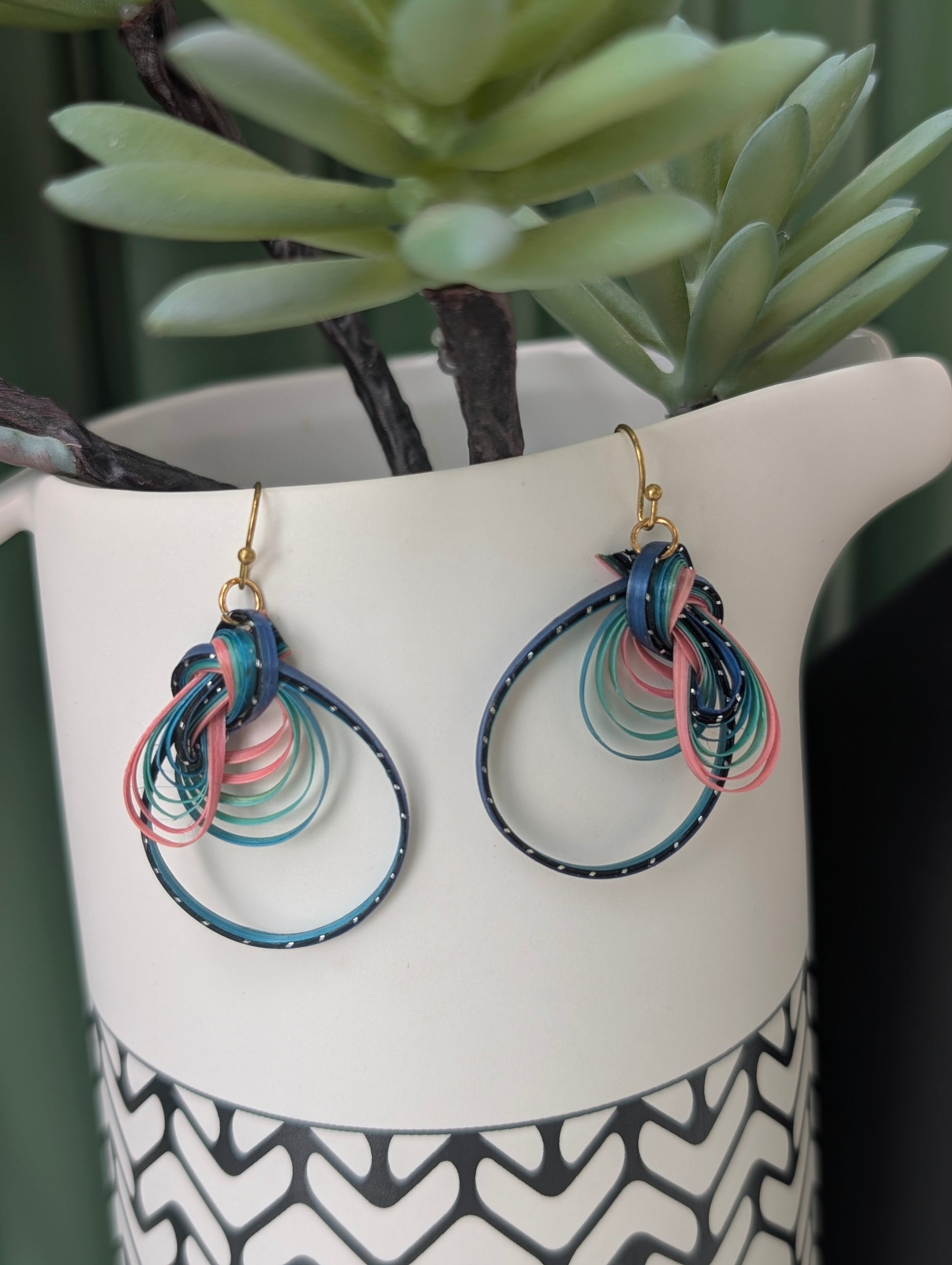 Colorful hoop earrings on a white stand with a plant in the background