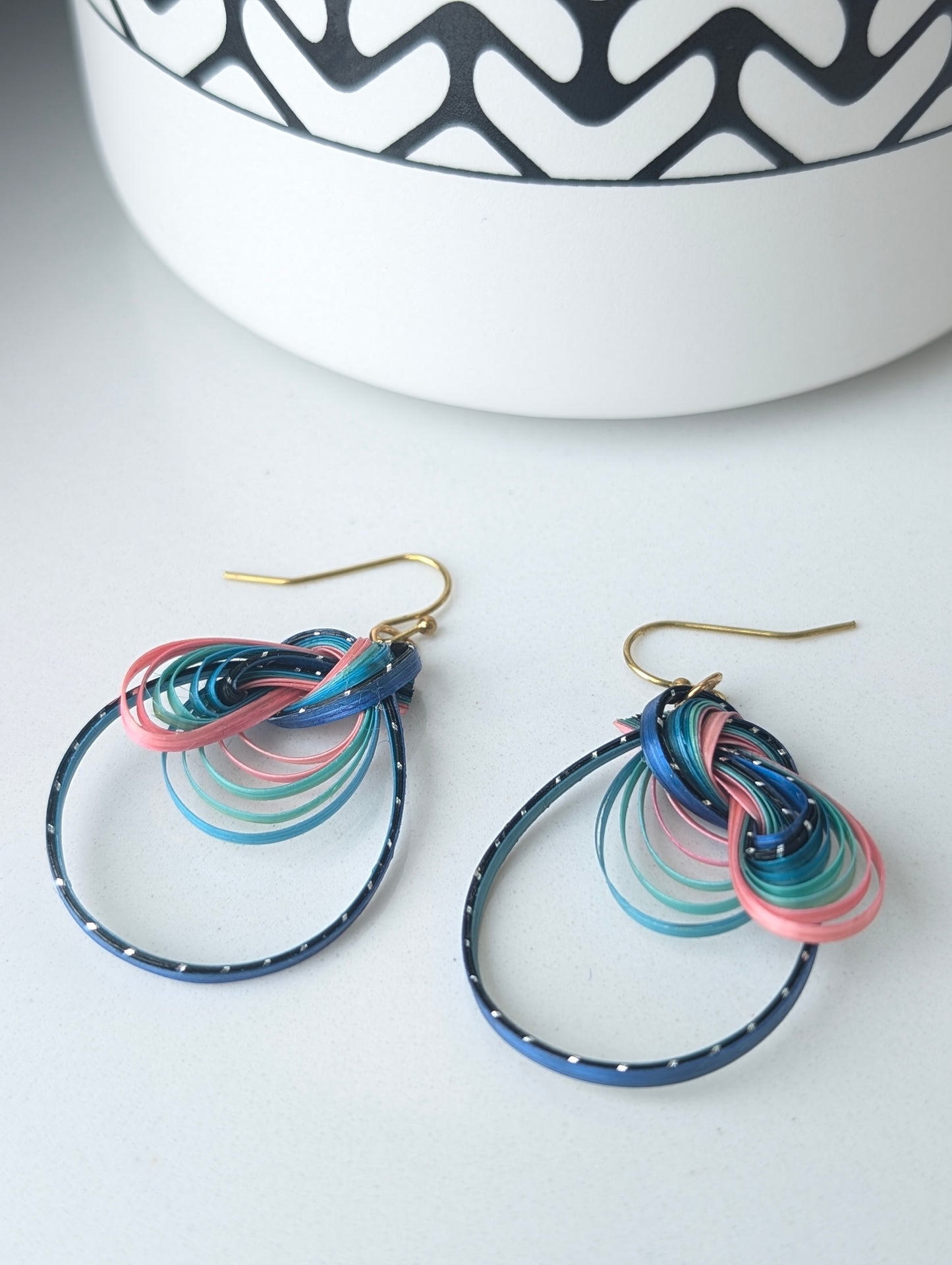 Colorful hoop earrings on a white surface with a decorative bowl in the background