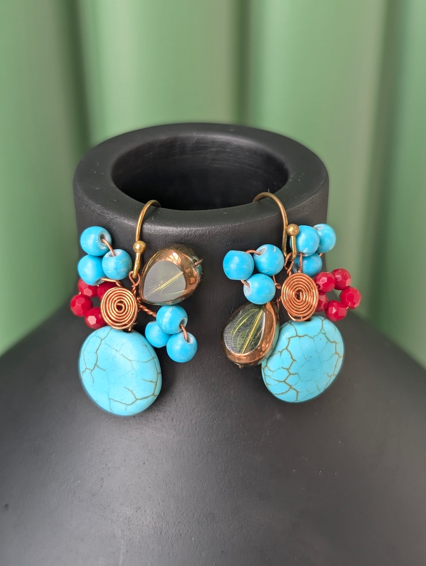 Pair of colorful earrings with turquoise stones on a dark surface.