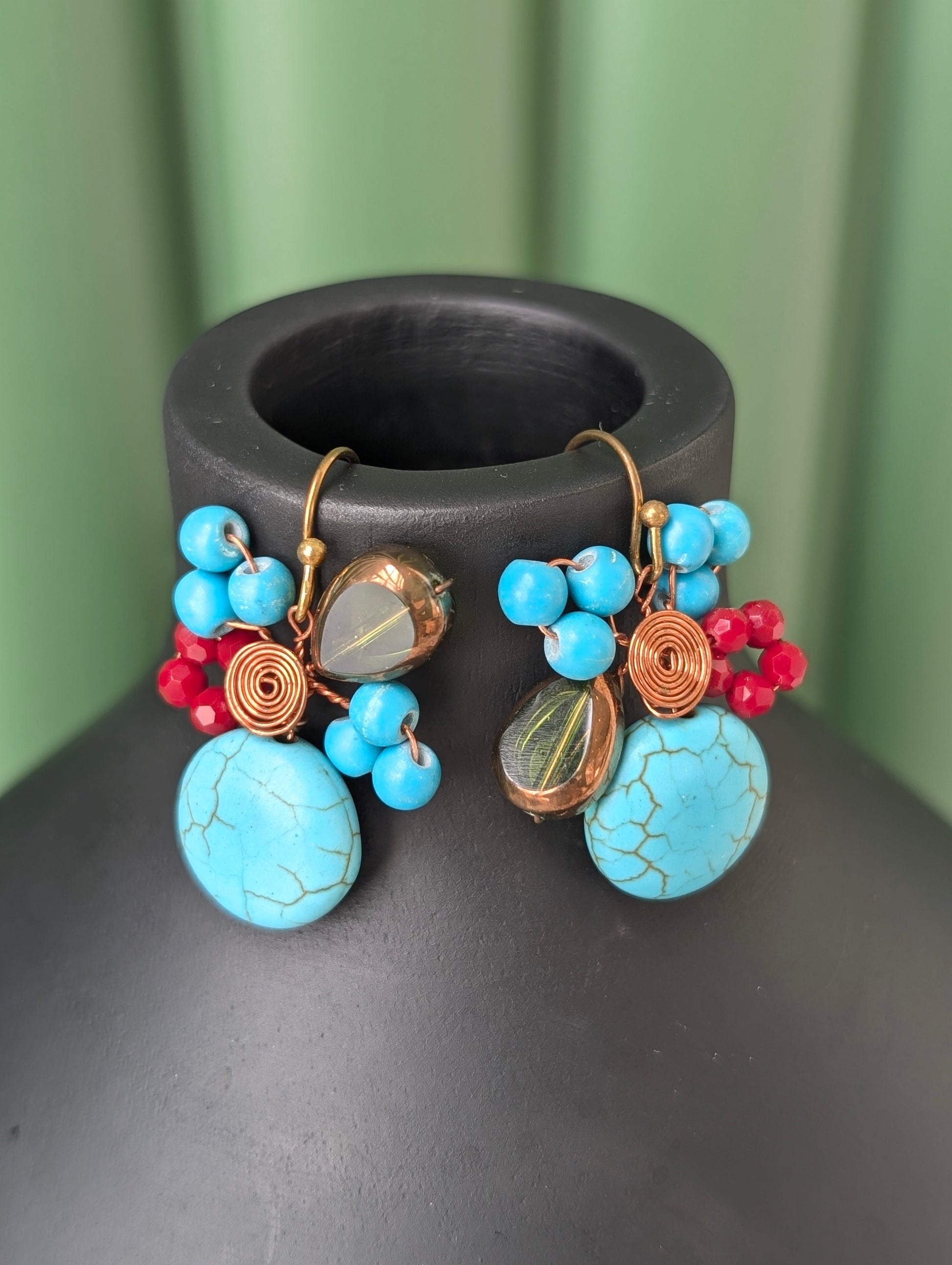 Pair of colorful earrings with turquoise stones on a dark surface.
