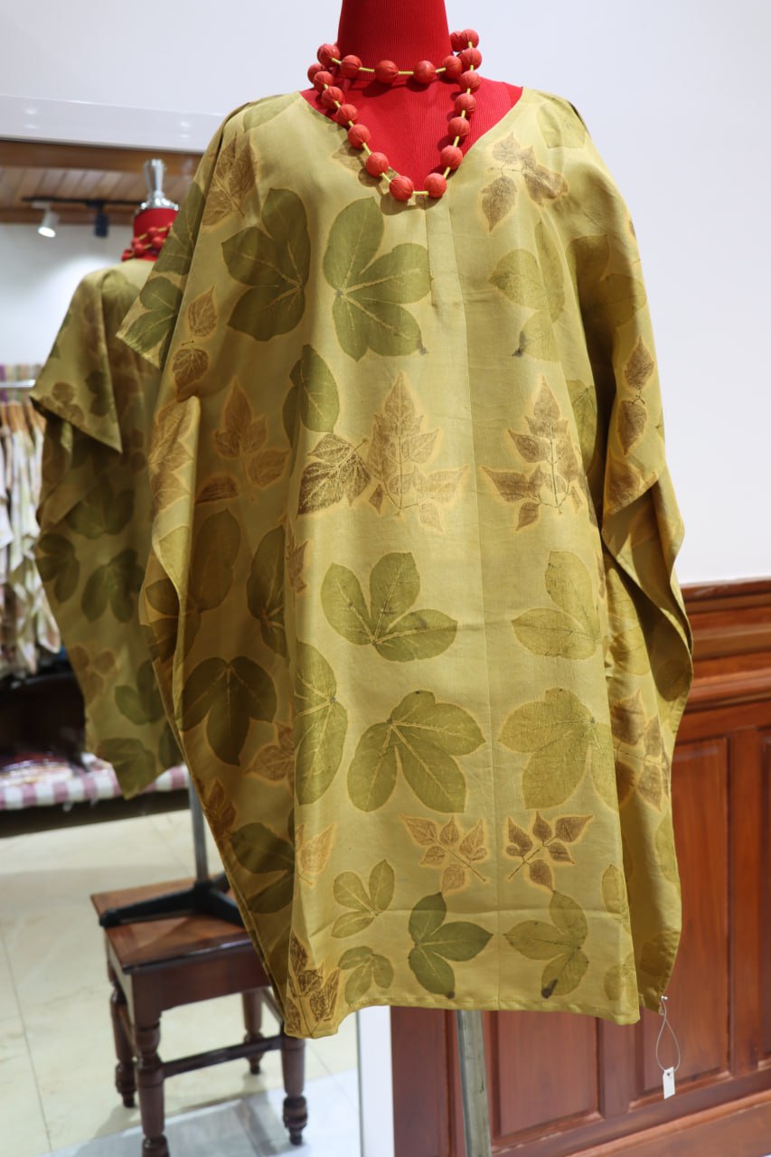 Green floral patterned dress on a mannequin with a red necklace against a white wall.