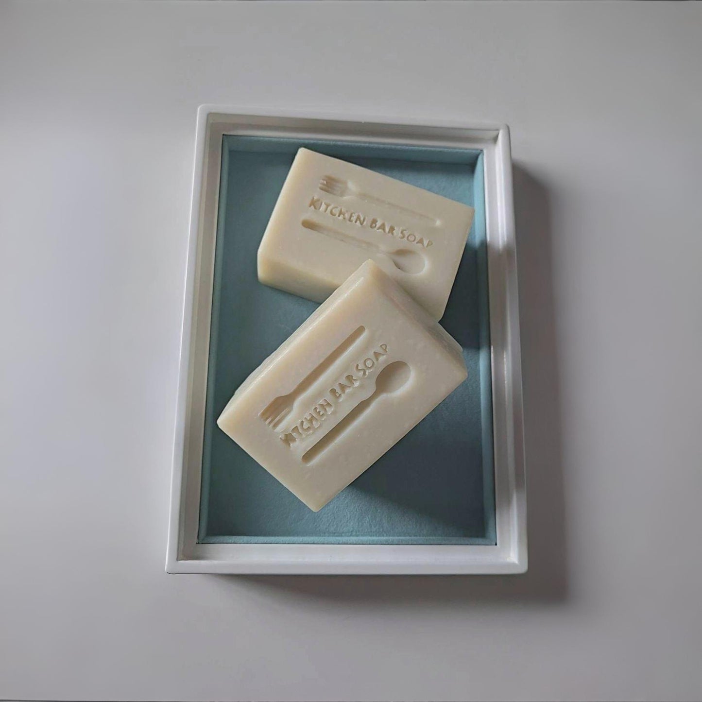 Two soap bars in a white frame with a light blue background